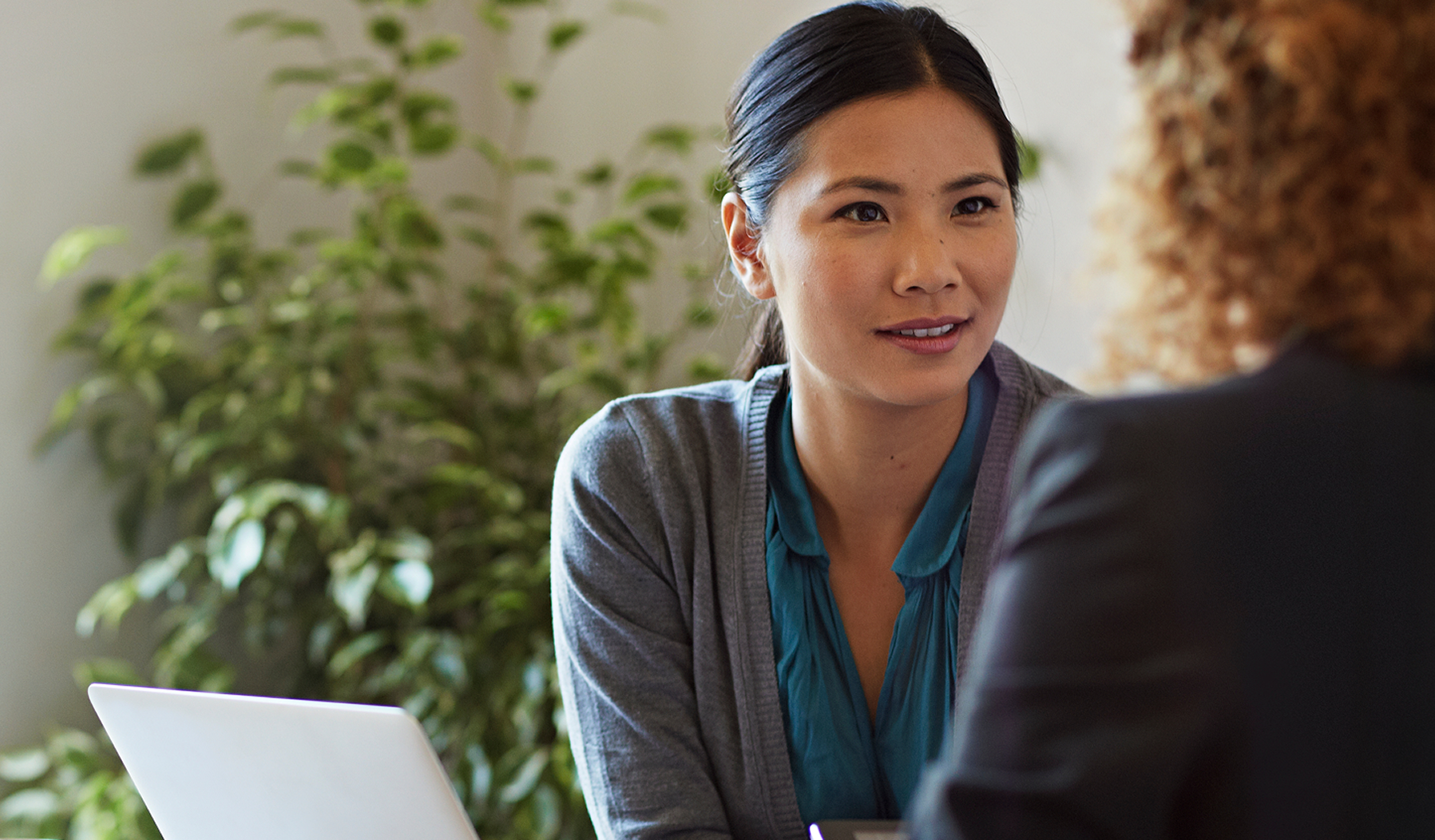 Woman speaking with a financial advisor in a bright room, seated across a desk with a laptop